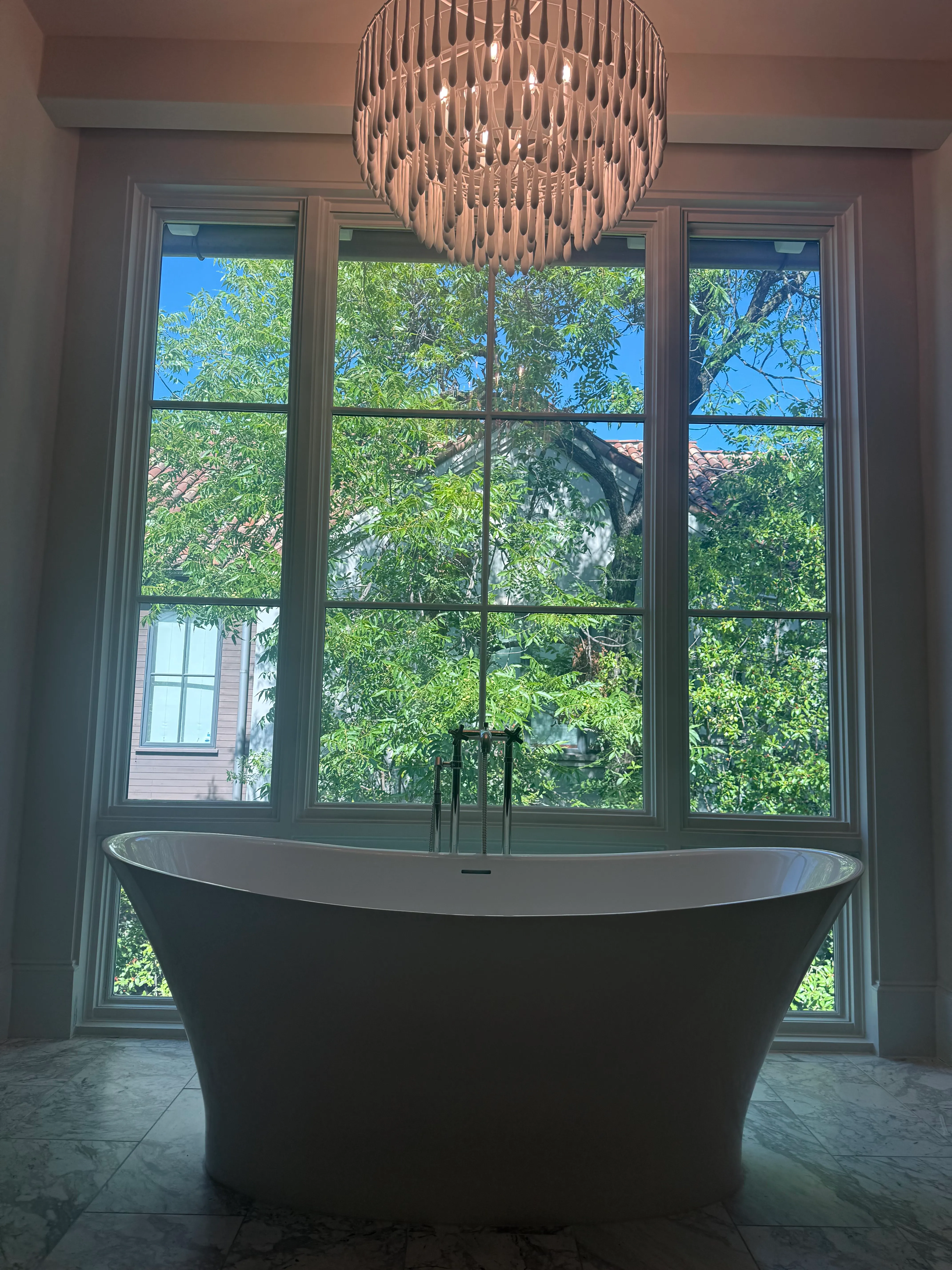Primary bath with an arched triple window in its clear state, looking out to trees